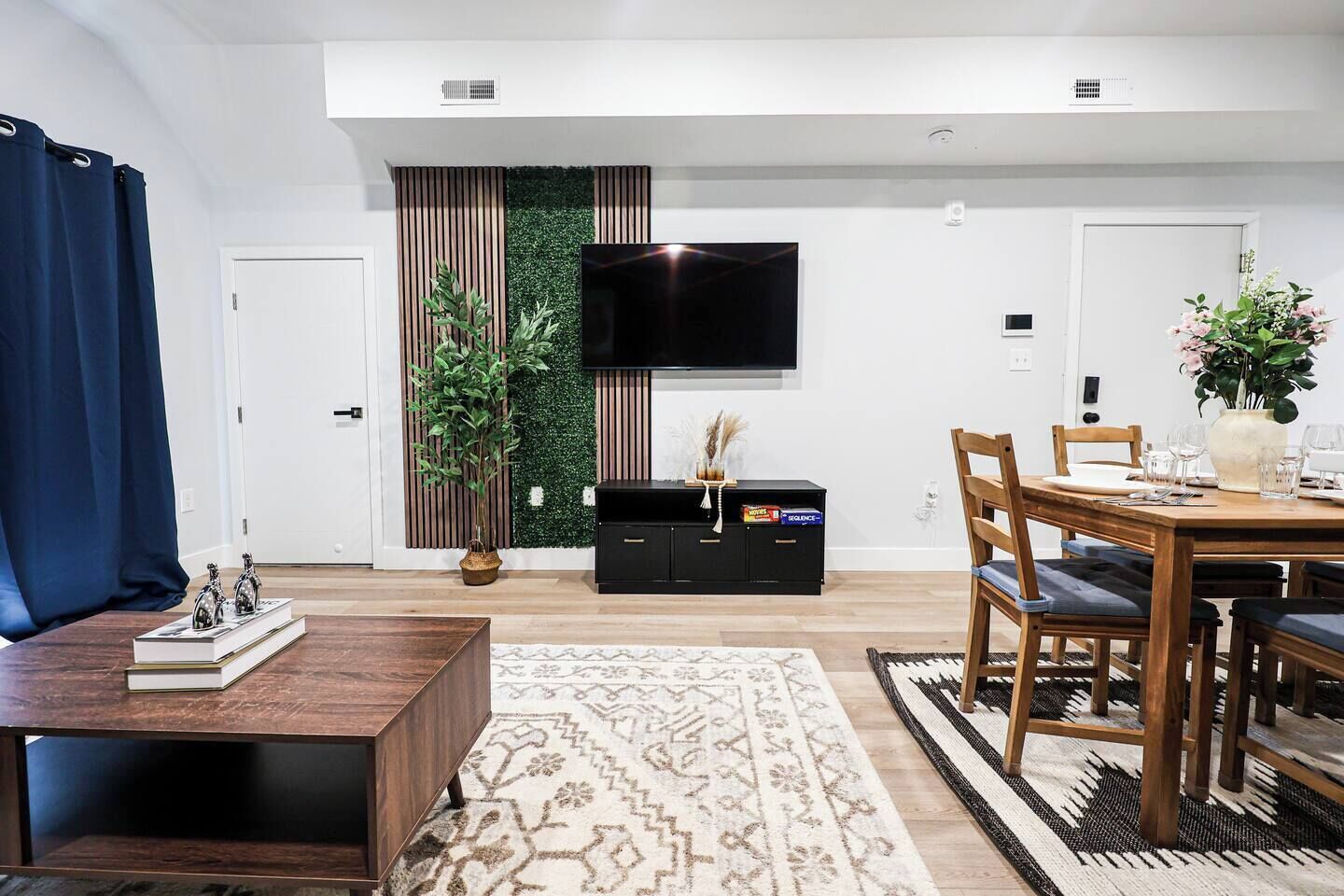 Een moderne woonkamer met een flatscreen televisie, houten meubels, een eettafel voor vier personen en een decoratieve plant.