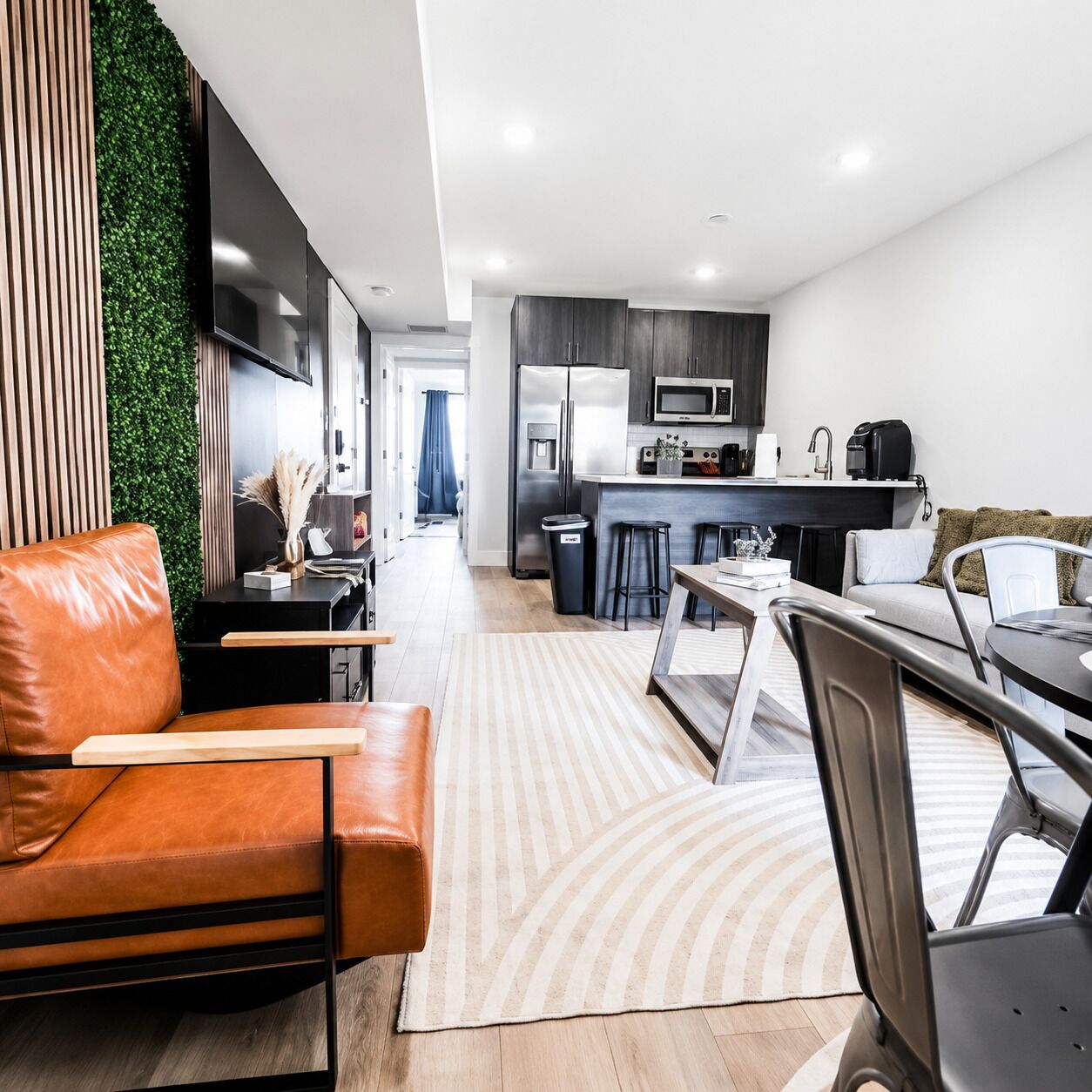 A modern kitchen with a refrigerator, microwave, and coffee maker. There is a dining area with a table and chairs.