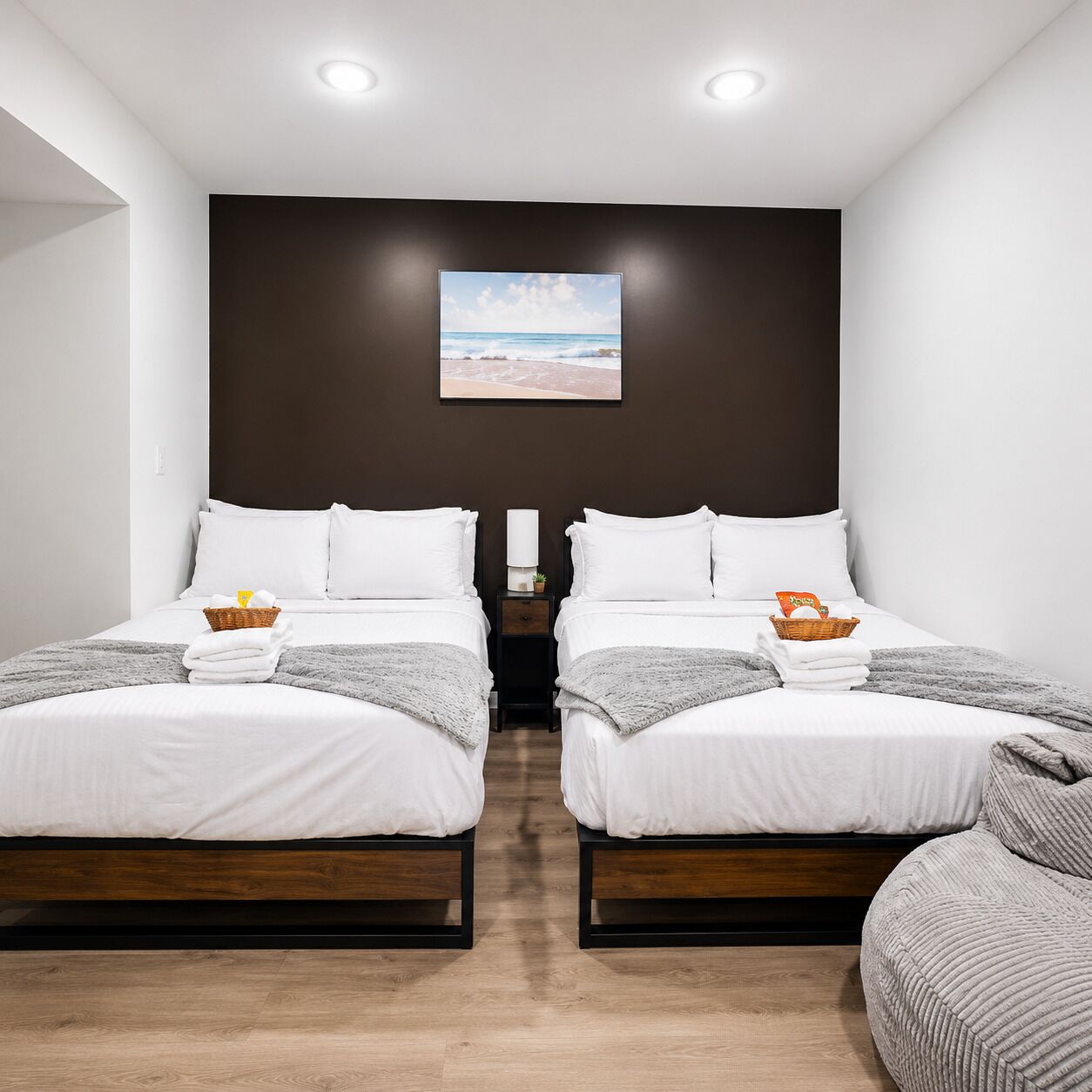 A hotel room with two beds, a nightstand, a wall-mounted picture, and a view of the beach.