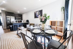 A modern kitchen with dark cabinets and stainless steel appliances, a dining area with a round table set for four, and a living space with a sofa and a large painting of Earth. - Sun-filled 2BR/1BA close to the Philadelphia Zoo and UPenn. Enjoy central air, in-unit laundry, and a sleek, modern kitchen — comfortably sleeps 6. Easy access to I-76 and I-676 for getting around the city. (Philadelphia)