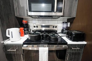 A compact kitchen with a microwave, stove, kettle, coffee maker, and toaster. - Modern 2BR near Philly Zoo & UPenn! Features central air, in-unit laundry, sleek kitchen & sleeps 6. Quick access to I-76/676 & top attractions. (Philadelphia)