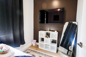 A room with a bed, a white shelving unit with decorative items, a television mounted on the wall, and a large mirror. - Modern 2BR near Philly Zoo & UPenn! Features central air, in-unit laundry, sleek kitchen & sleeps 6. Quick access to I-76/676 & top attractions. (Philadelphia)