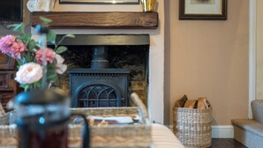 A cozy living room with a fireplace, a wicker basket, and a vase with flowers. - Beautiful 2BD Cottage in the Cotswolds (Bourton-on-the-Hill)