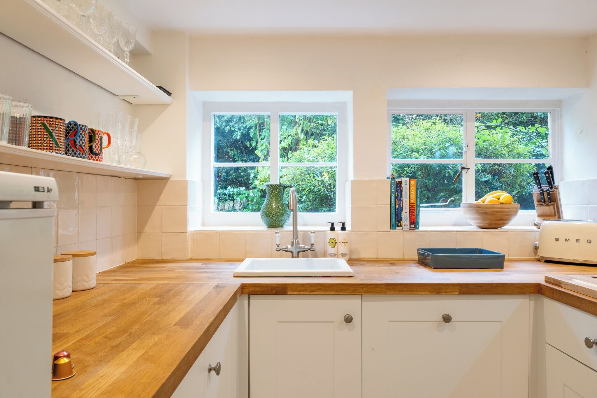 A kitchen with a wooden countertop, white cabinets, a sink, and a window with a view of greenery.