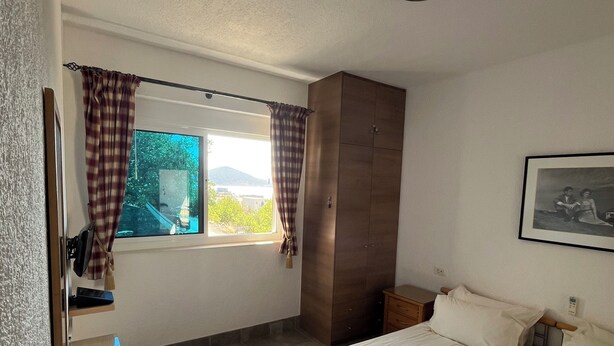 Une chambre avec deux lits, un bureau avec une chaise, une armoire, une fenêtre avec des rideaux et un tableau encadré au mur.
