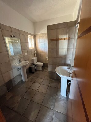 Un baño con dos lavamanos, un inodoro y un espejo.