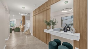Un interior moderno con un panel de madera en la pared, una consola blanca con adornos y una escalera que conduce a otra habitación.