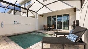 A pool area with a hot tub, lounge chairs, and a table with chairs.
