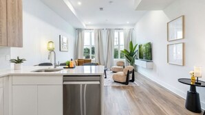 A modern kitchen with a central island, a dining area with a sofa and chairs, and a view of the outdoors through large windows.