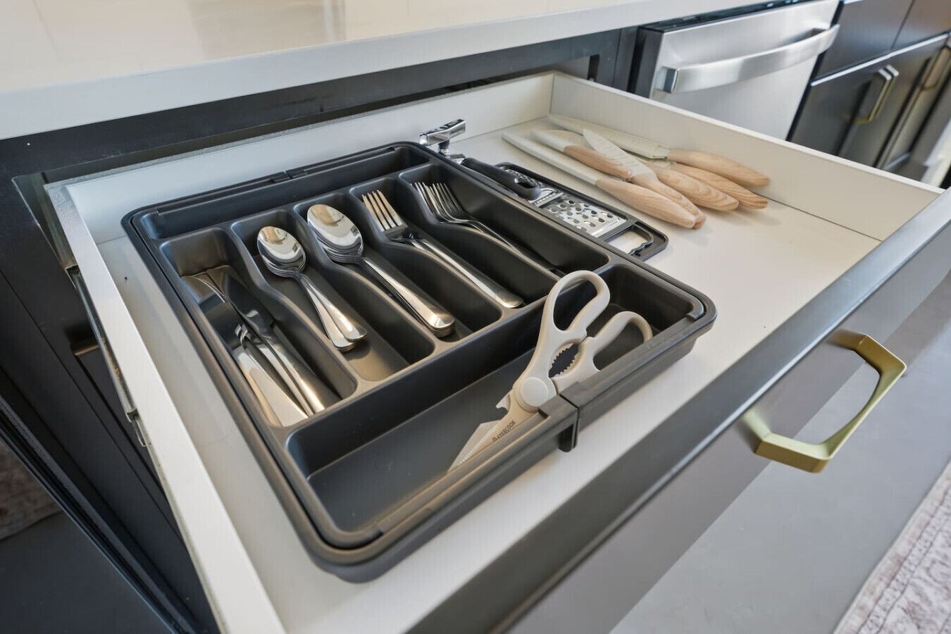 Un tiroir de cuisine contenant des ustensiles, notamment une râpe, des couteaux et une paire de ciseaux.