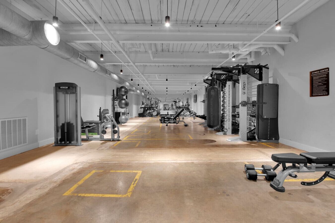 Ein Fitnessstudio mit verschiedenen Trainingsgeräten, darunter Laufbänder, Kraftgeräte und Kurzhanteln.