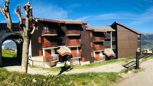 A modern building with multiple balconies and a stone archway. - Apartment in Le Christiana on Ski Slopes (Aime-la-Plagne)
