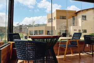 Un área de estar moderna al aire libre con sillas de mimbre y una mesa de madera, con vistas a un edificio residencial y un cielo despejado.