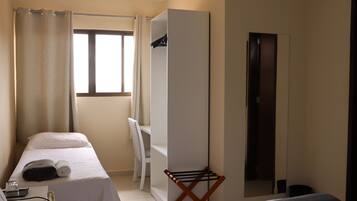 Habitación de hotel con dos camas, una ventana con cortinas, un armario, un espejo y una pequeña mesa con un vaso y una toalla.