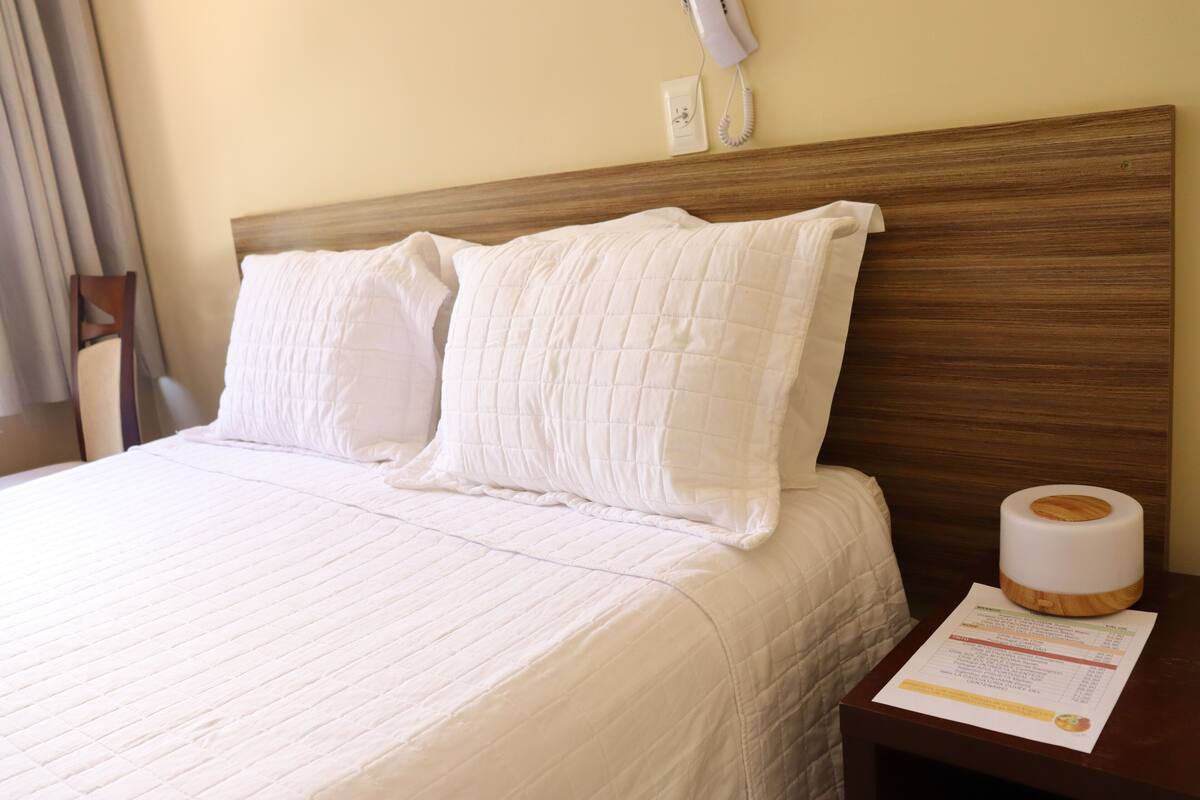 A hotel room with a neatly made bed, a wooden headboard, a bedside table with a tissue box, and a wall-mounted phone.