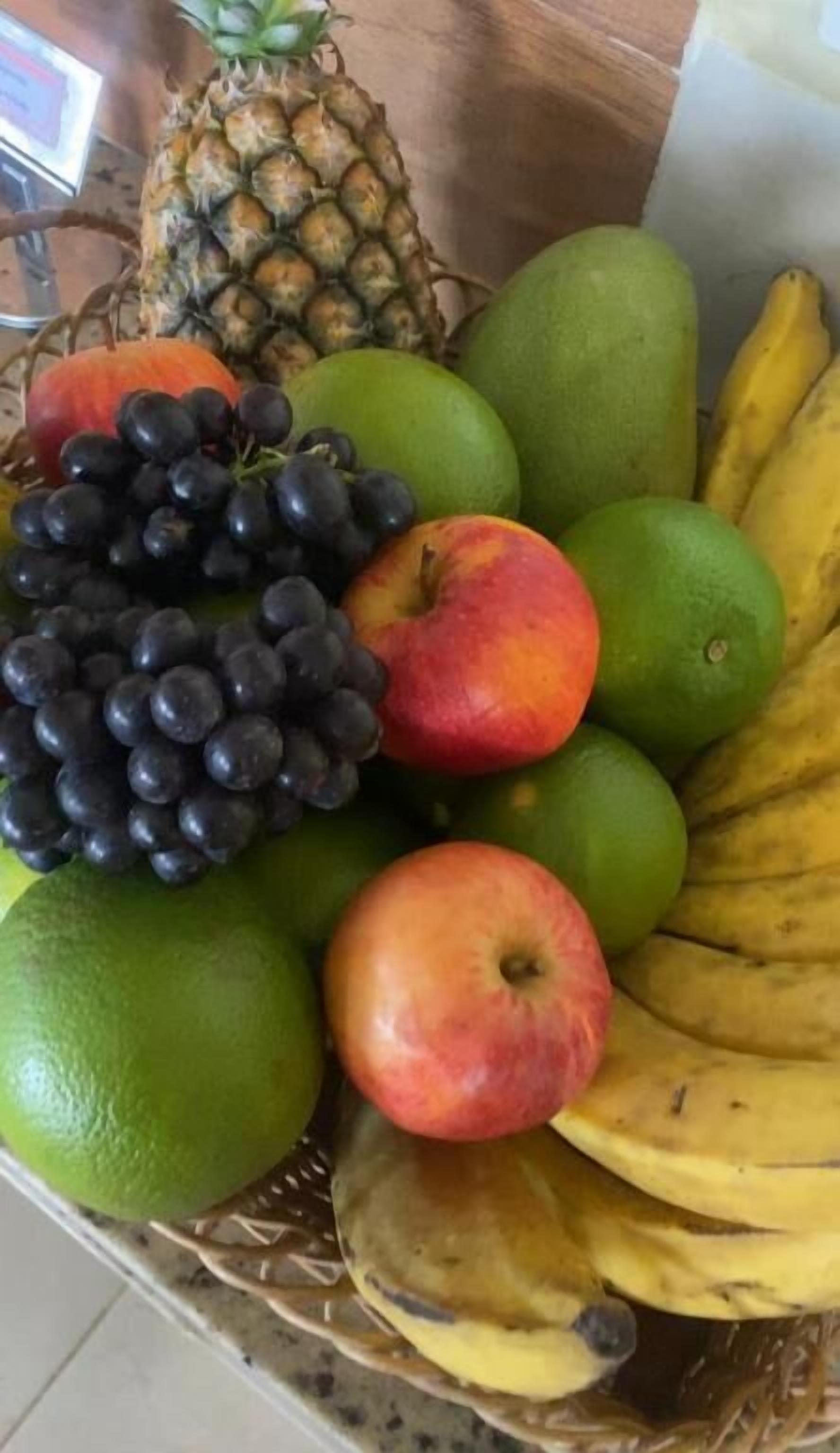 A fruit basket containing apples, grapes, limes, bananas, and a pineapple.