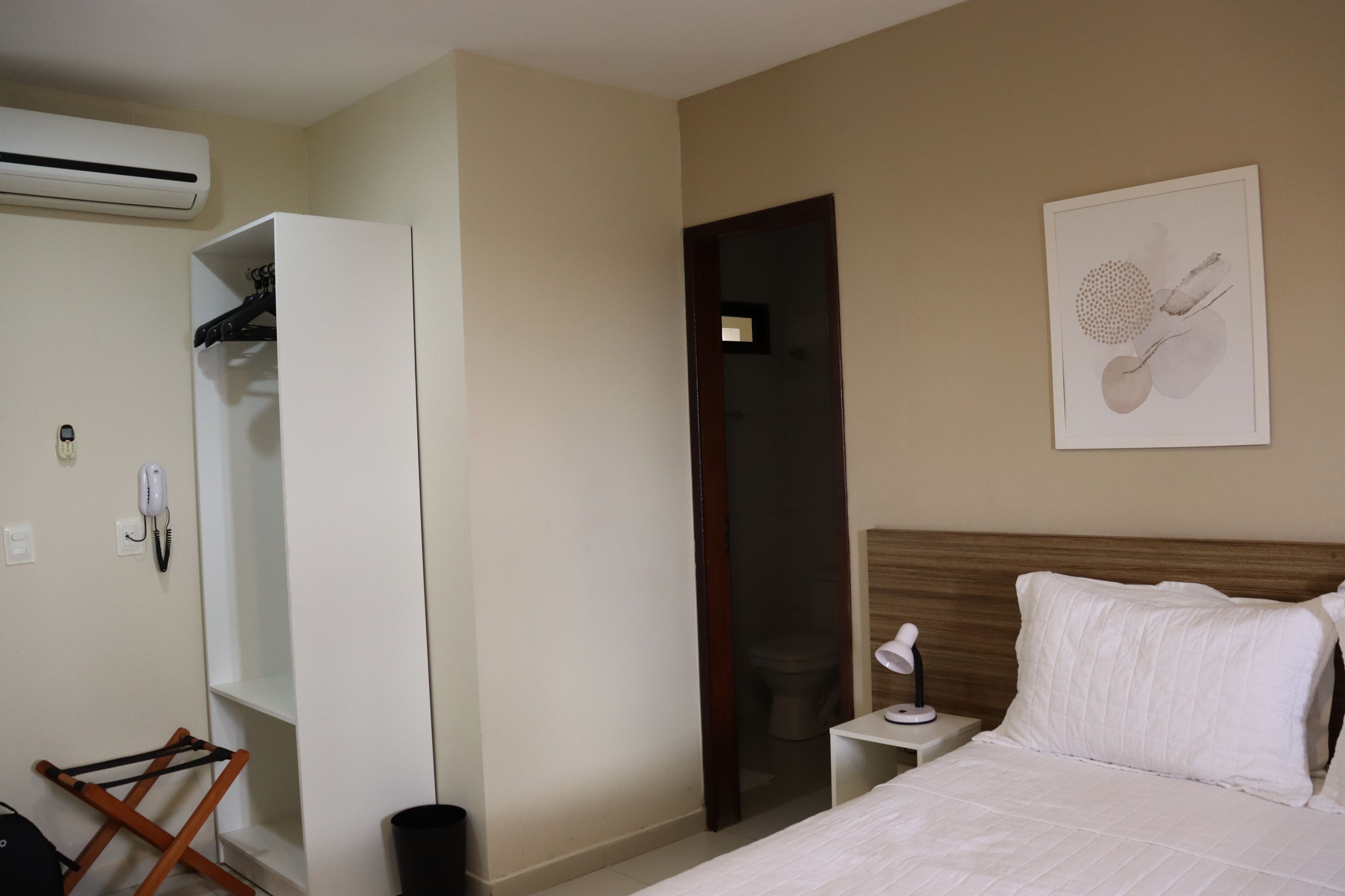 Une chambre d’hôtel comprenant un lit, une table de chevet, une armoire blanche, une porte et une œuvre d’art accrochée au mur.