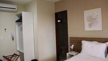 Une chambre d’hôtel comprenant un lit, une table de chevet, une armoire blanche, une porte et une œuvre d’art accrochée au mur.