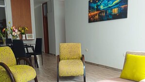 A living room with a pink sofa, yellow patterned chairs, a dining area with a table and chairs, and a painting on the wall. - Casa Estancia Jaén * Jaén Country House *. (Jaén)