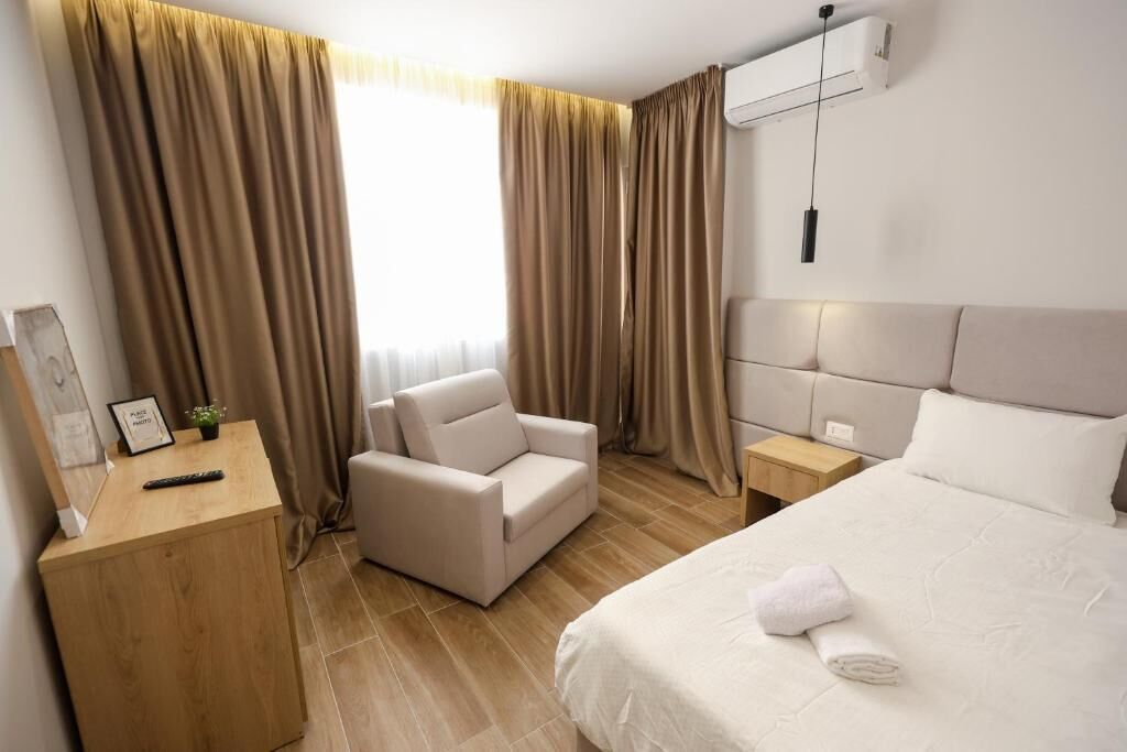 A hotel room with a bed, a chair, a bedside table, and a nightstand.