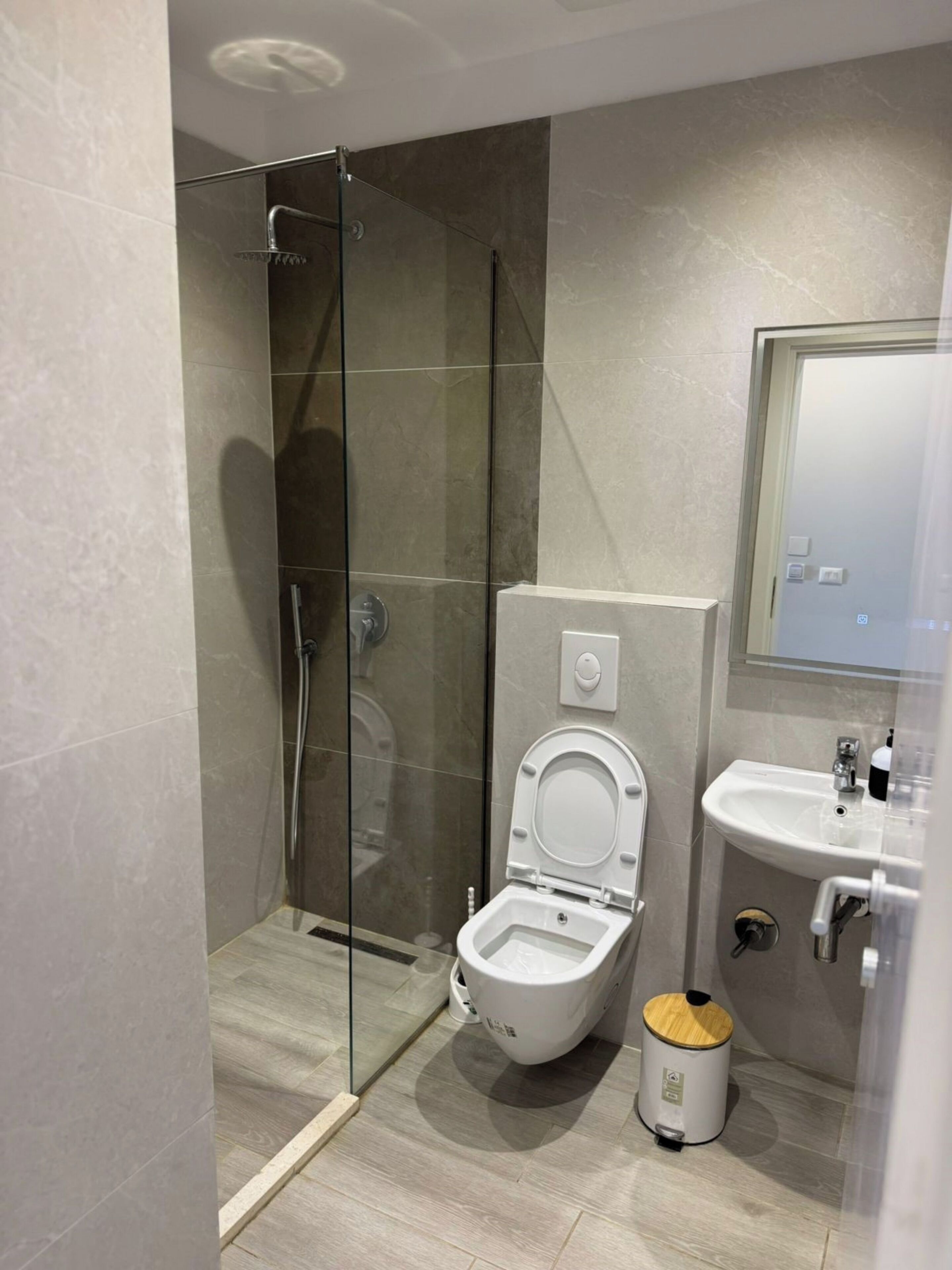 Un baño moderno con ducha de vidrio, inodoro, lavabo y un cubo de basura.