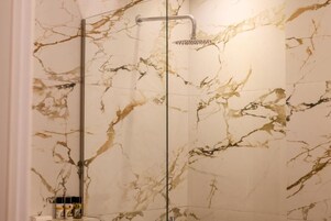 Una ducha con cerramiento de vidrio y pared con diseño de mármol.