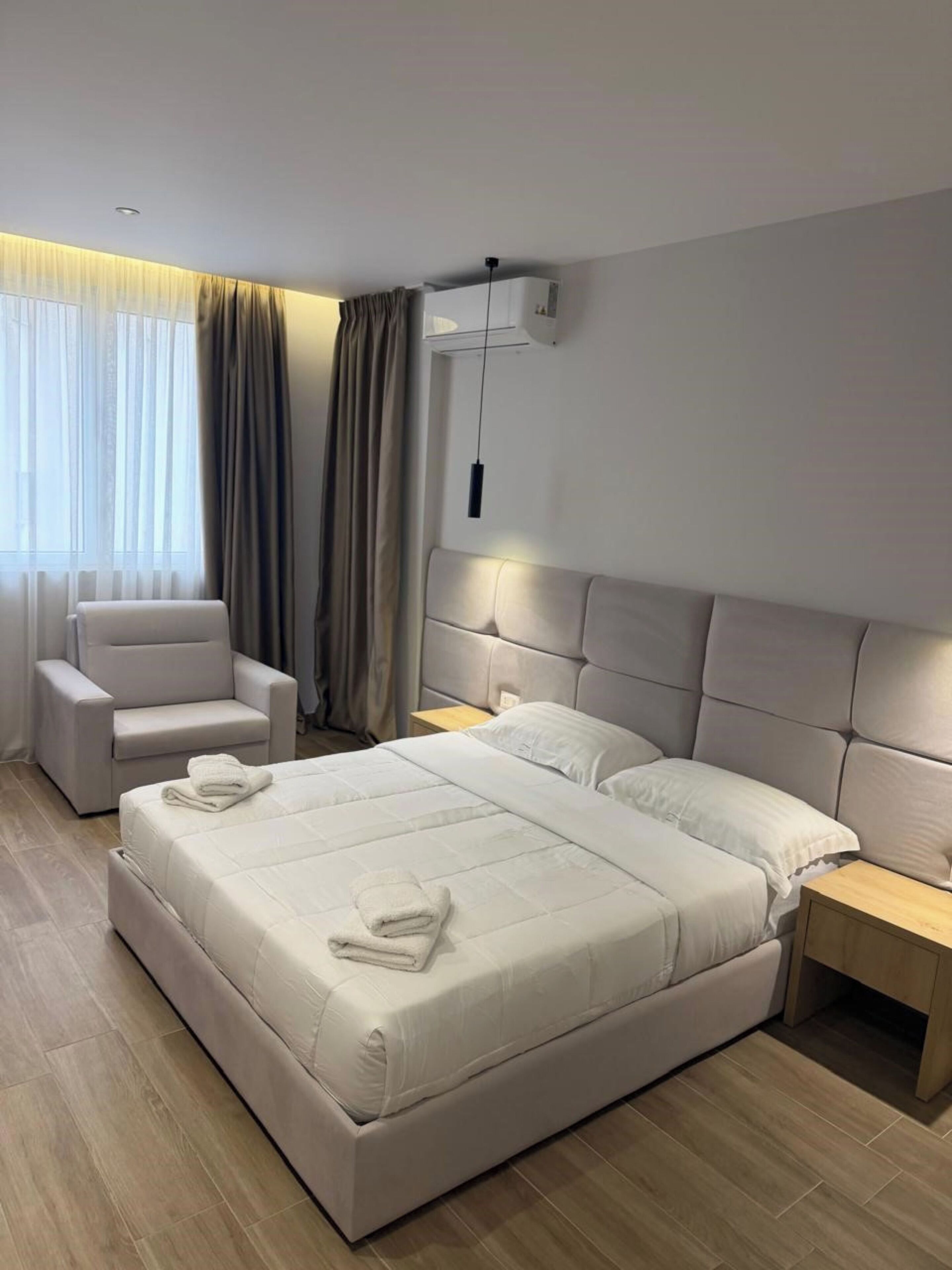 Camera d'albergo moderna con un letto grande, una sedia, un comodino e una finestra con tende.