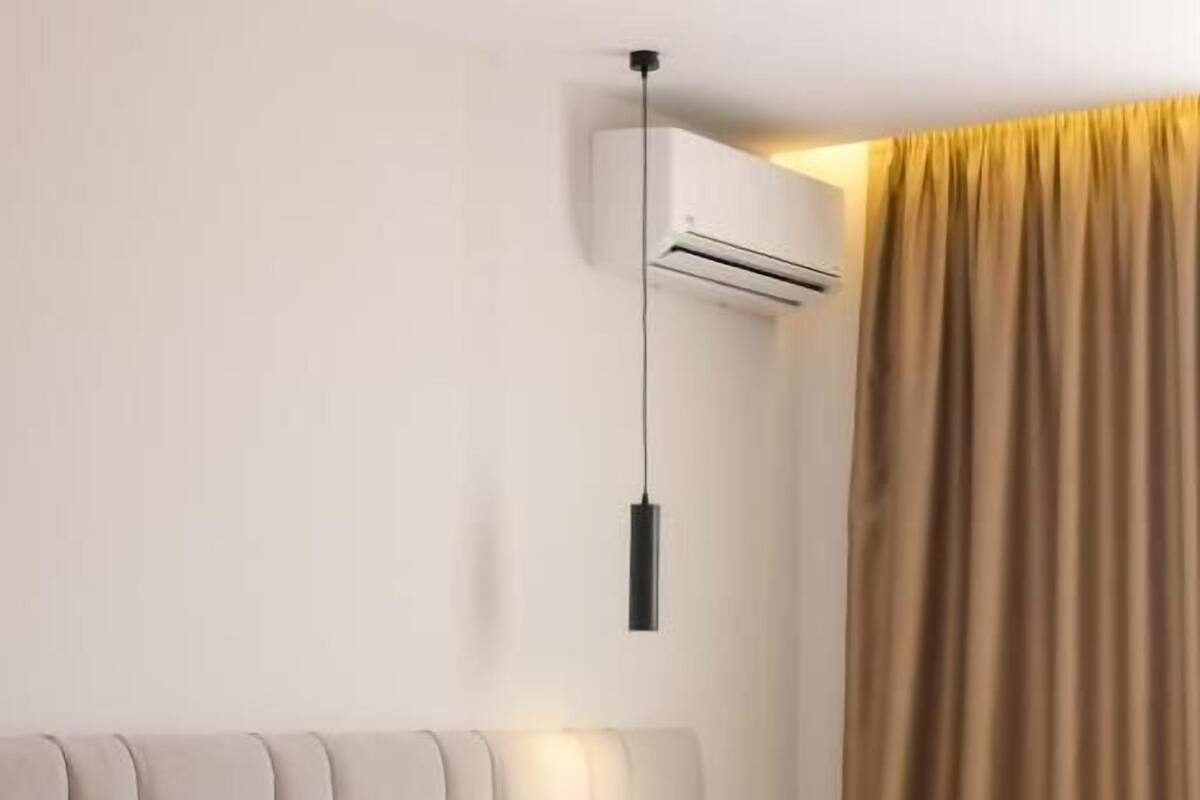 Una habitación de hotel con cama, mesita de noche, lámpara, equipo de aire acondicionado y cortina.