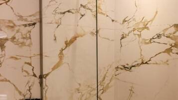 Une salle de bain avec une douche à parois de verre, des murs en marbre et des toilettes.