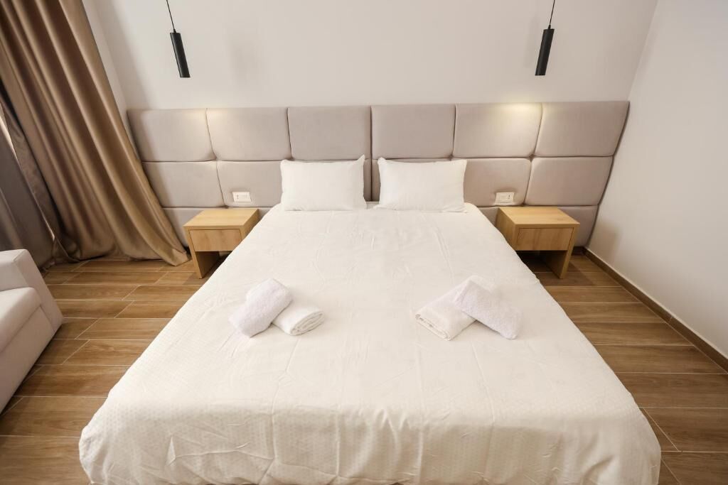 A hotel room with a large bed, two bedside tables, a headboard, and a curtain.