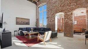 A spacious living area with a large dark sofa, a wooden coffee table, and a red patterned rug. - Unique, Historic 2BD Apt w/ Study (Greenville)