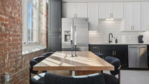 A modern kitchen with a wooden dining table, black chairs, white cabinets, and stainless steel appliances. - Unique, Historic 2BD Apt w/ Study (Greenville)