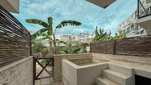 A modern outdoor area with a concrete pool, steps leading to a balcony, and a view of the surrounding buildings. - TWT CONDOS (Tulum)