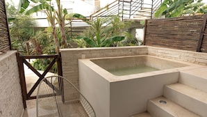 A spa area with a hot tub, steps leading to it, and a chair. - TWT CONDOS (Tulum)