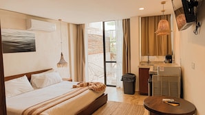 A hotel room with a bed, a small table, a chair, a TV, and a view of the outdoors. - TWT CONDOS (Tulum)