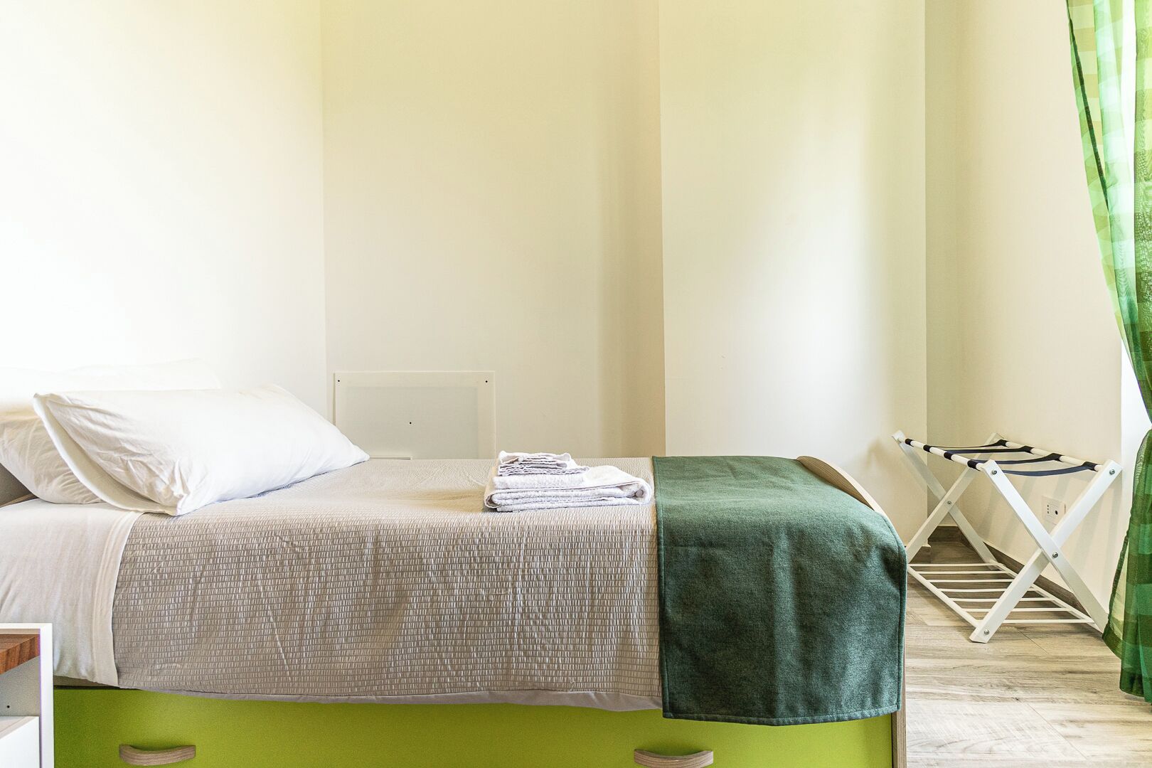 Una cama bien tendida con un cabecero verde, una toalla doblada y una manta verde.