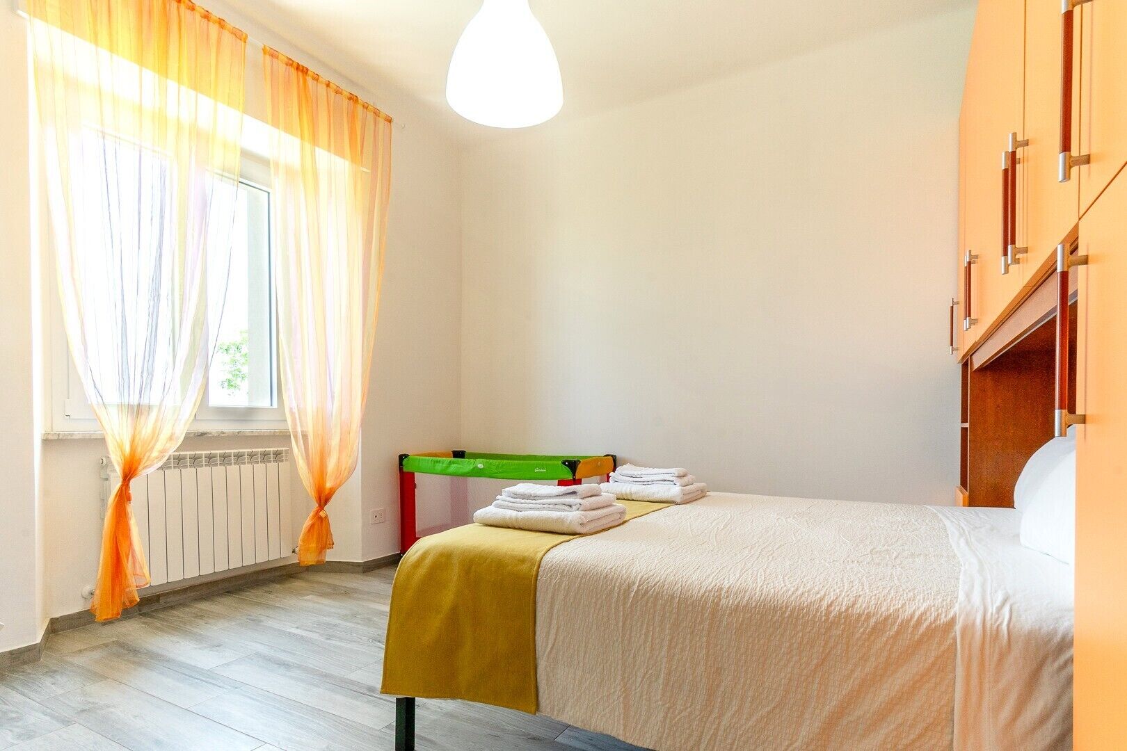 Et hotelværelse med seng, et lille bord med håndklæder, en radiator og et vindue med gardiner.
