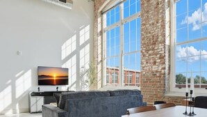 A spacious living area with a large gray sectional sofa, a wooden dining table with chairs, and a ceiling fan. - Bright and Elegant Abode Near DT GVL (Greenville)