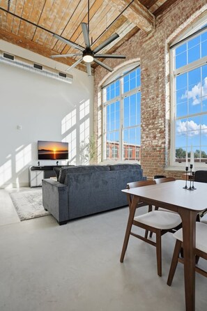 Uma sala ampla com um sofá seccional cinza grande, uma mesa de jantar de madeira com cadeiras e um ventilador de teto.