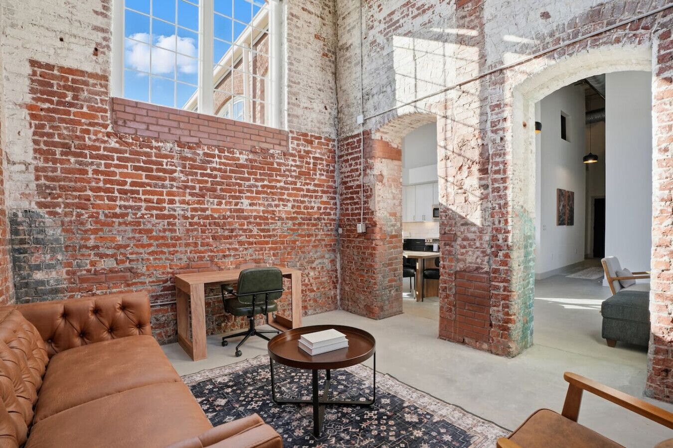 A spacious room with exposed brick walls, a leather sofa, a wooden desk, and a dining area.