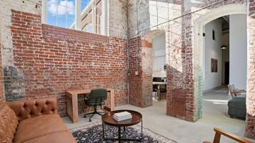 A spacious room with exposed brick walls, a leather sofa, a wooden desk, and a dining area.