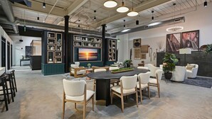Een ruime kamer met een grote eettafel, omringd door stoelen, een boekenkast en een televisietoestel.