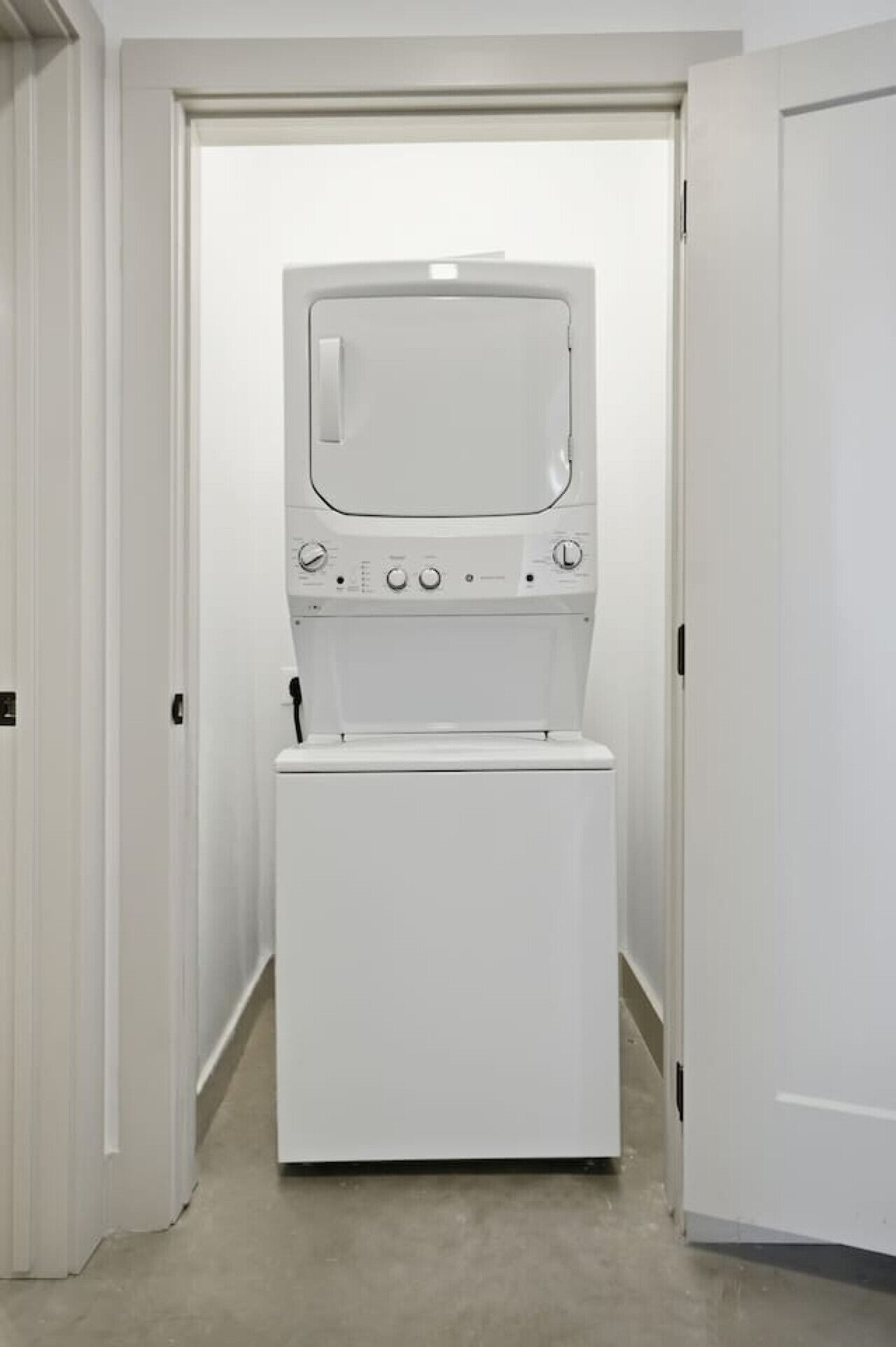 Una sala de lavandería con lavadora y secadora, paredes blancas y una puerta que da a otra habitación.