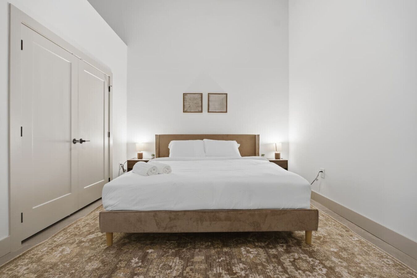 Uma cama bem arrumada com lençóis brancos, uma cabeceira de madeira e duas luminárias de cabeceira.