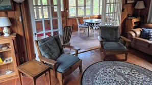 Ein gemütliches Zimmer mit Holzwänden, einem karierten Sofa, einem runden Tisch und einem Essbereich mit Stühlen.