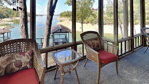 A covered outdoor seating area with wicker furniture and a glass table, overlooking a lake and beach. - Reel It In | Epic Views, Dock & Pier, Game Room (Dandridge)
