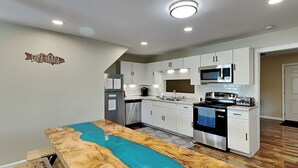 A modern kitchen with white cabinets, stainless steel appliances, and a unique wooden island with a blue river design. - Reel It In | Epic Views, Dock & Pier, Game Room (Dandridge)