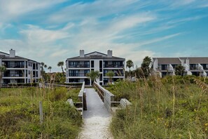 A pathway leading to a modern multi-story building with balconies, surrounded by natural vegetation. - New Listing! Beautifully Renovated Direct Oceanfront Condo! (Saint Augustine Beach)