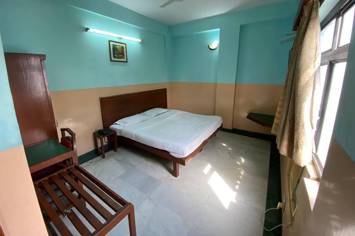 Quarto com cama, escrivaninha, cadeira, ventilador de teto e janela com cortinas.