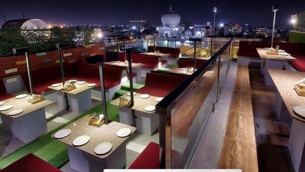 Un ristorante sul tetto con diversi tavoli e sedie, una vista sulla città sullo sfondo e un cielo notturno sereno.